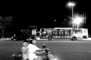 一张黑白照片 夜晚的街道 人们骑自行车 一辆公交车驶过。