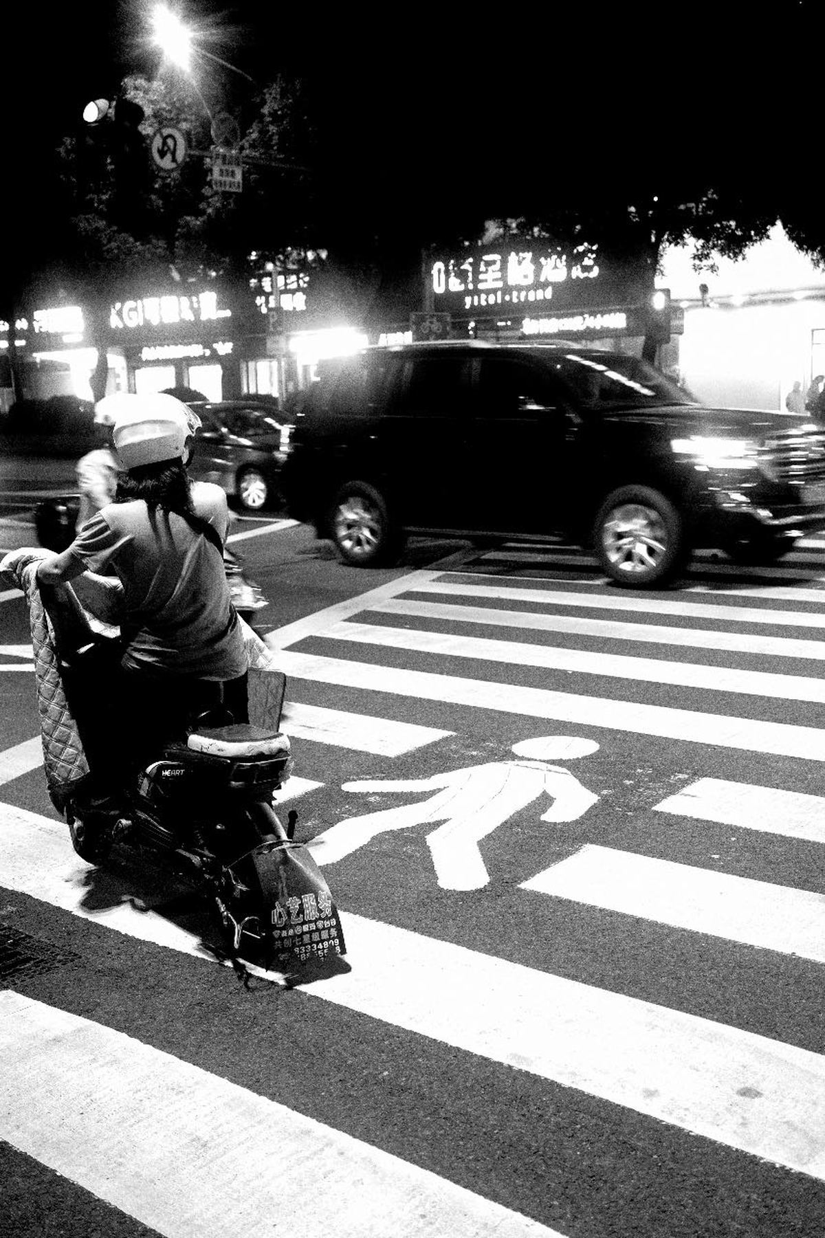 一个黑白照片 夜晚的交叉口 人们骑着摩托车和汽车在街道上行驶。