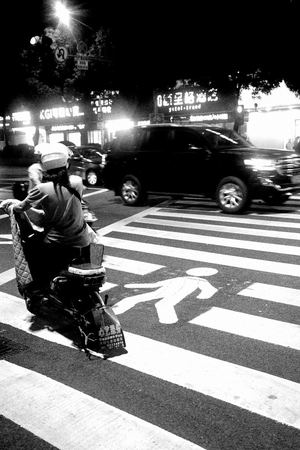 一个黑白照片 夜晚的交叉口 人们骑着摩托车和汽车在街道上行驶。