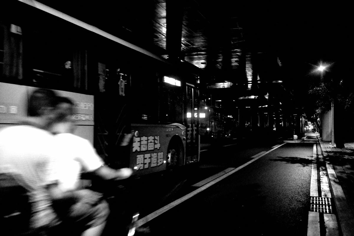 一张黑白照片 一个人在晚上骑自行车穿过城市街道