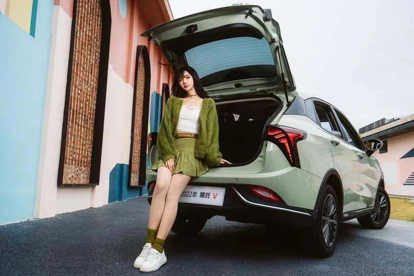 一个年轻女子坐在汽车敞开的行李箱里 行李箱里还放着行李。