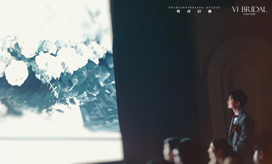 一个人站在一个房间的大窗户前 周围有很多人群。