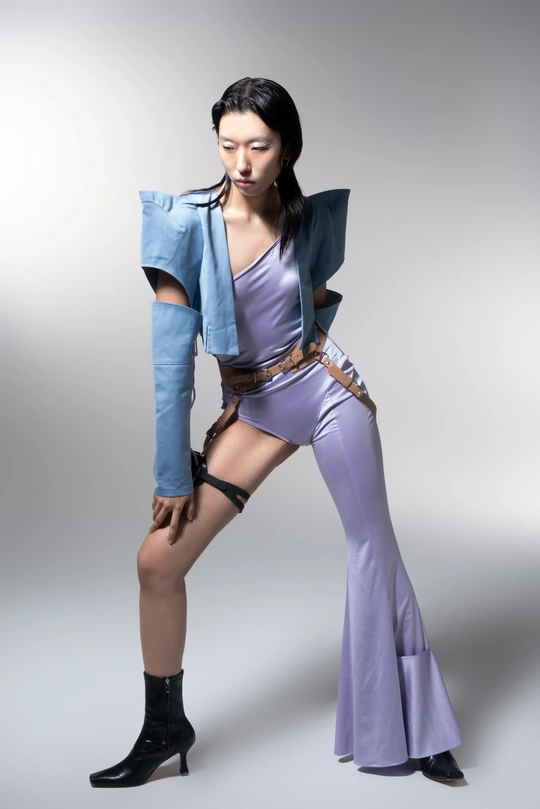 一位年轻的女模特穿着蓝色夹克、紫色连衣裙和靴子 在白色背景上摆姿势。