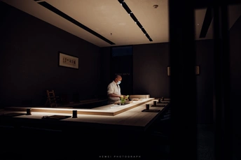 一个男人坐在黑暗的房间里的桌子旁 房间前面的桌子上放着寿司