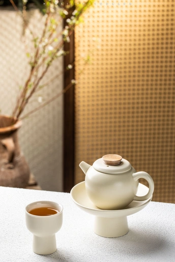 一个白色的杯子和一个白色的盘子放在一张白色的桌子旁边 旁边还有一个茶壶。