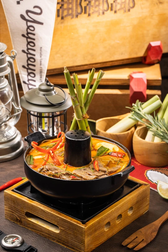 一个木制桌子顶部放着一锅食物和一个碗蔬菜。