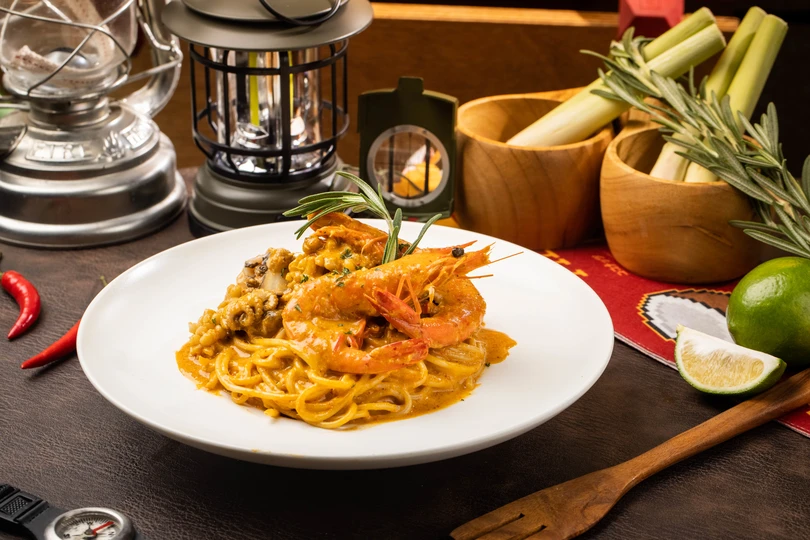 一张带有白色盘子的食物表格 其中包括意大利面、虾和一碗辣椒汤。