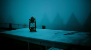 一个黑暗的房间 有一张床和一张桌子 桌子上有一盏点亮的灯笼和蜡烛。