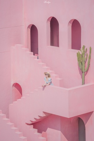 一个小女孩坐在粉红色楼梯顶端的一所粉色房子里 房子四周都是粉色墙壁。