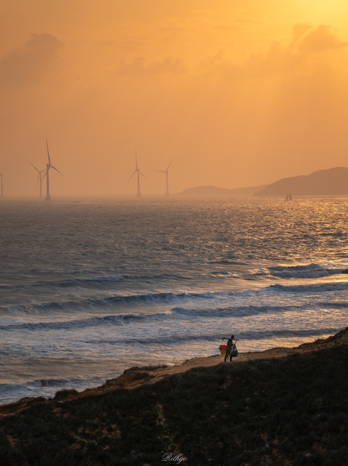 夕阳西下 几人在远处风力发电机下沿着海滩漫步。