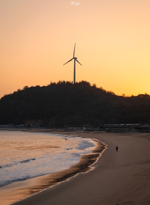 夕阳西下 太阳在日落时在沙滩上的风车后面。