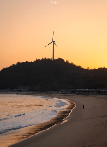 夕阳西下 太阳在日落时在沙滩上的风车后面。