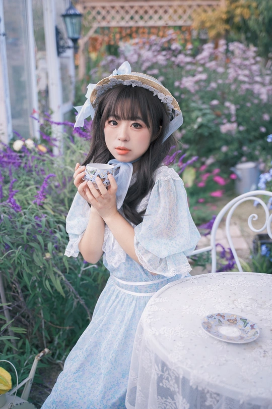 一位穿着蓝色连衣裙和帽子 手里拿着一杯茶的小女孩