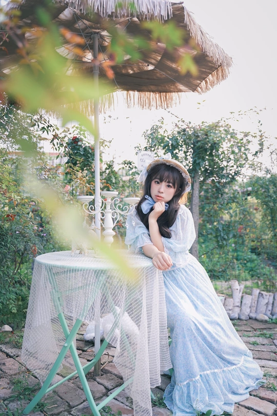 一个穿着白色连衣裙的年轻女子坐在花园里在伞下