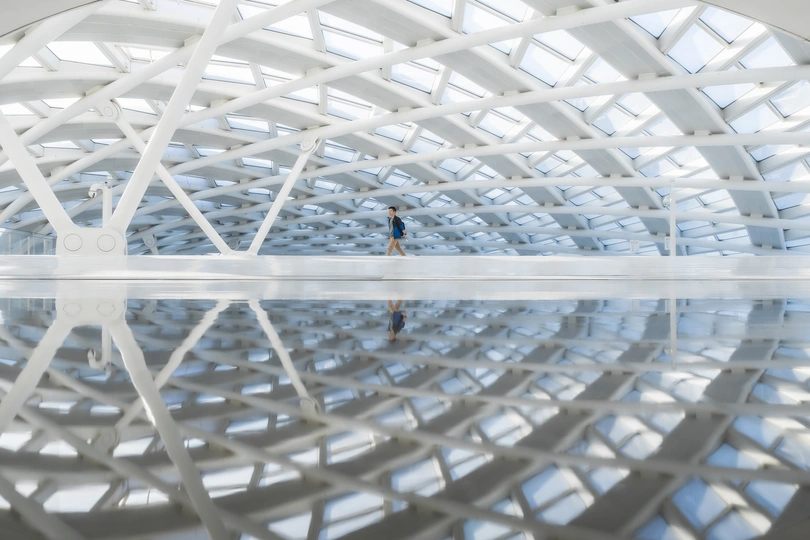 一个人站在一个大型白色结构内的水中 有反射。