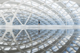 一个人站在一个大型白色结构内的水中 有反射。