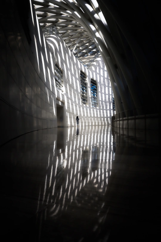 一个人站在一个有光线透过窗户照射进来 墙壁上有阴影的隧道里。