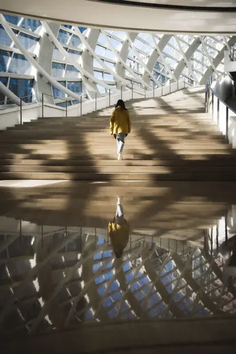 一个人骑着滑板在大型建筑的楼梯上跑下来 建筑物的其他人的倒影。