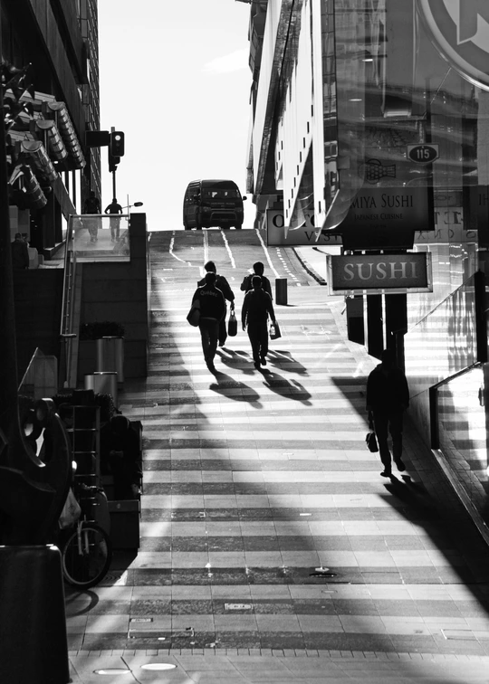 一些男人走在建筑物旁边的一条长人行道上。