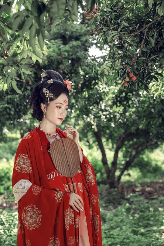 一位身穿传统红色连衣裙、撑着雨伞的年轻女子站在树下
