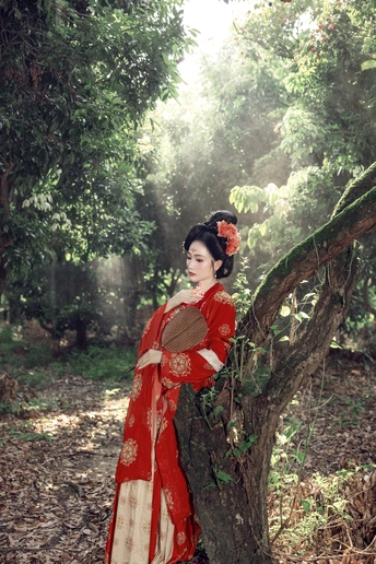 一个穿着传统红色连衣裙的女人站在树林里的一棵树旁