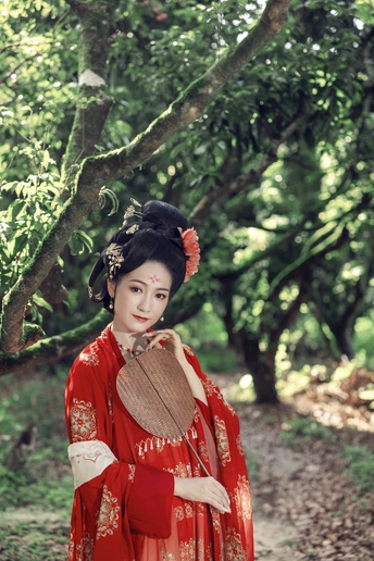 一位身穿传统红色连衣裙、撑着雨伞的年轻女子站在森林的小路上