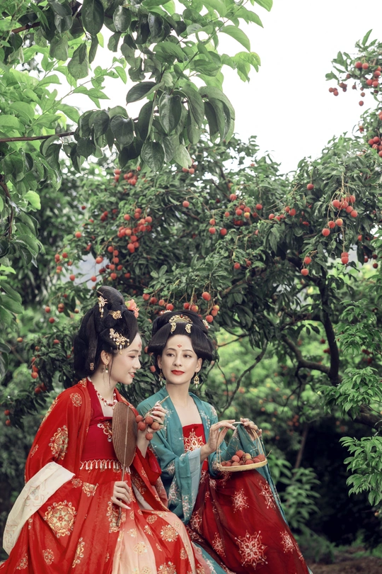 一对身着传统服饰的年轻女子在一个绿树成荫的花园里摆姿势