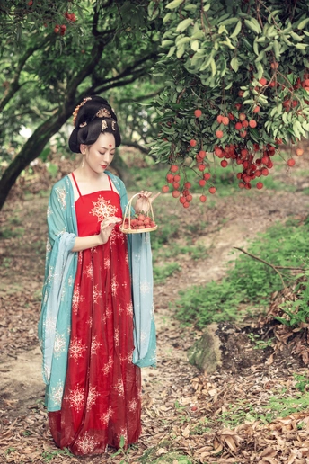 一个穿着红色连衣裙的年轻女子站在森林里 手里拿着一篮红色浆果