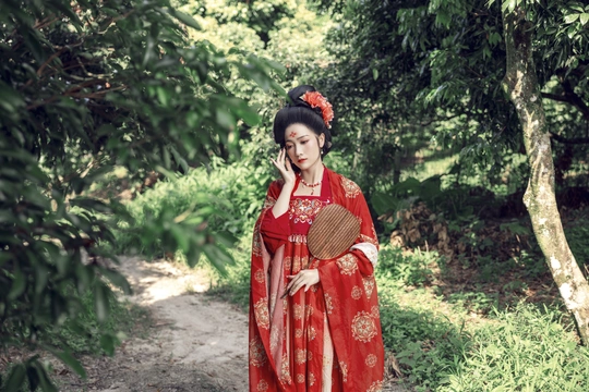 一个穿着红色连衣裙、拿着手机的女人沿着树林里的小路走着