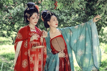 一对身着传统服装的年轻女子站在树下 身穿红白相间的连衣裙