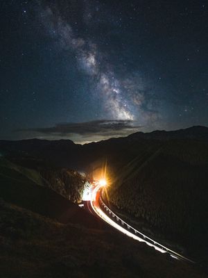 夜晚穿越山脉 天空中繁星闪烁 路上有一辆车。