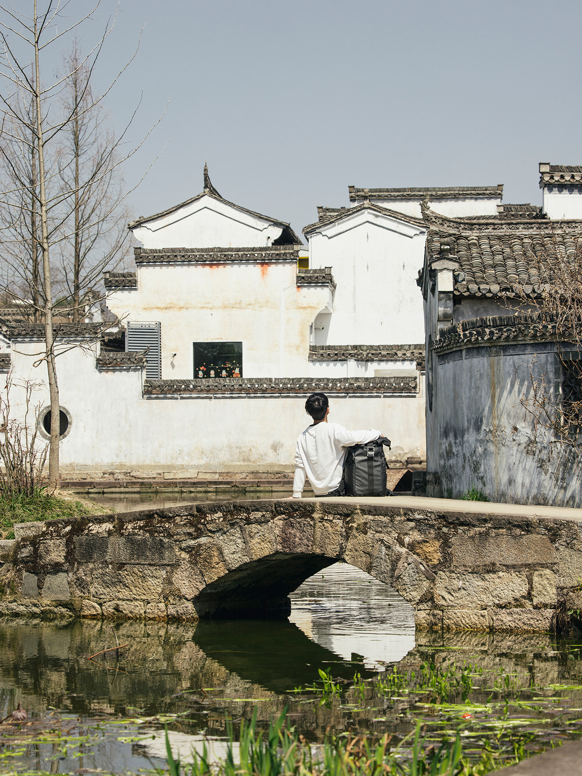 一个坐在小桥上的一座小池塘边的男人 背景是古老的建筑。