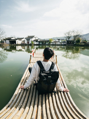 一个背着背包的年轻男子坐在河上的木桥上