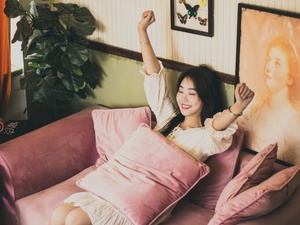 一个年轻的女人坐在粉红色的沙发上 枕头和一个放在床上的枕头