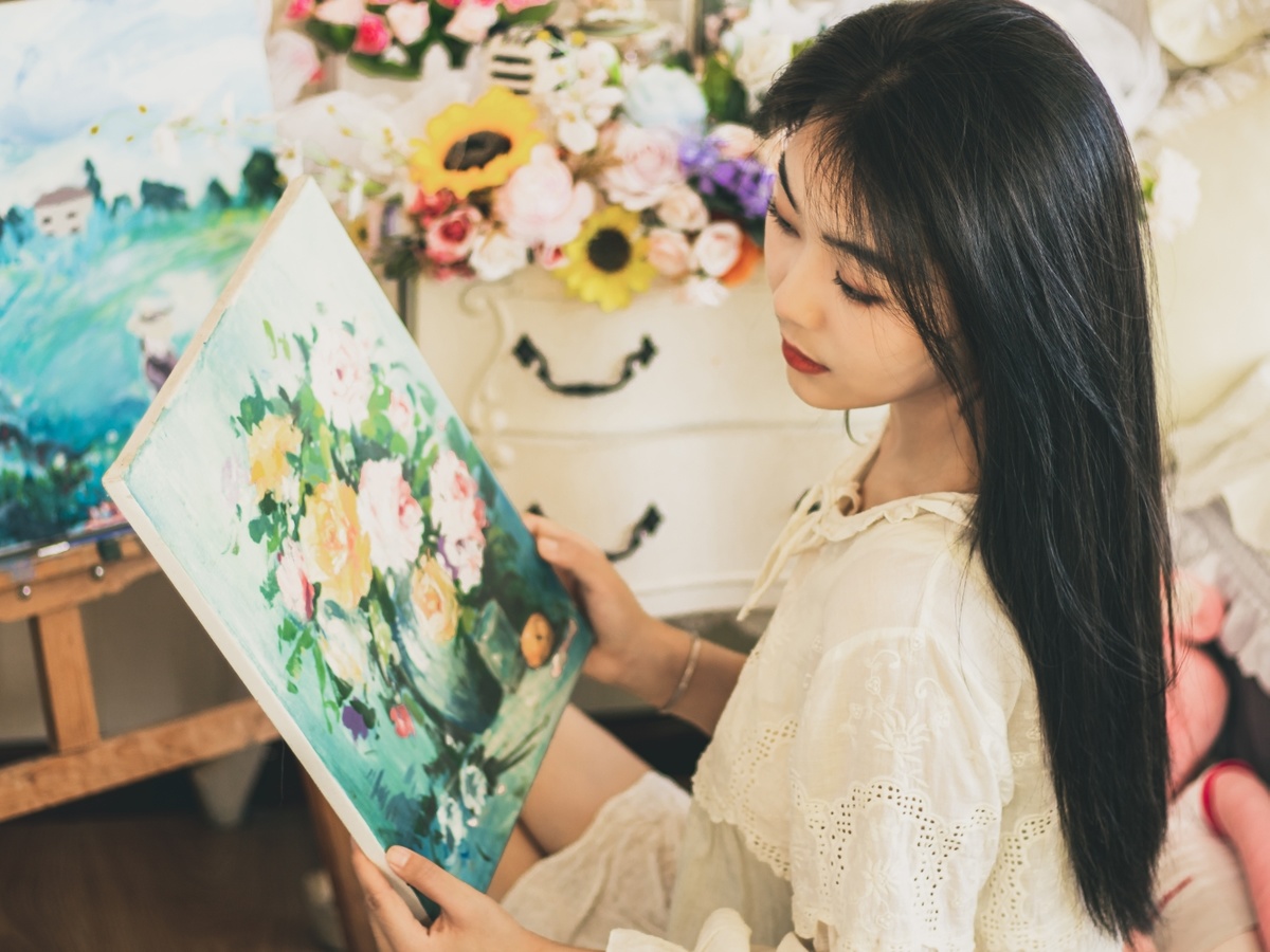 一个小女孩坐在地板上的画布前 画布上有花和一幅女人的画