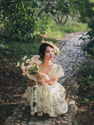 一个穿着白色连衣裙、手里拿着一束鲜花的漂亮年轻女子坐在鹅卵石路上