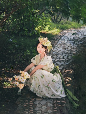 一个穿着漂亮连衣裙的年轻女子坐在花园里的石头小路上