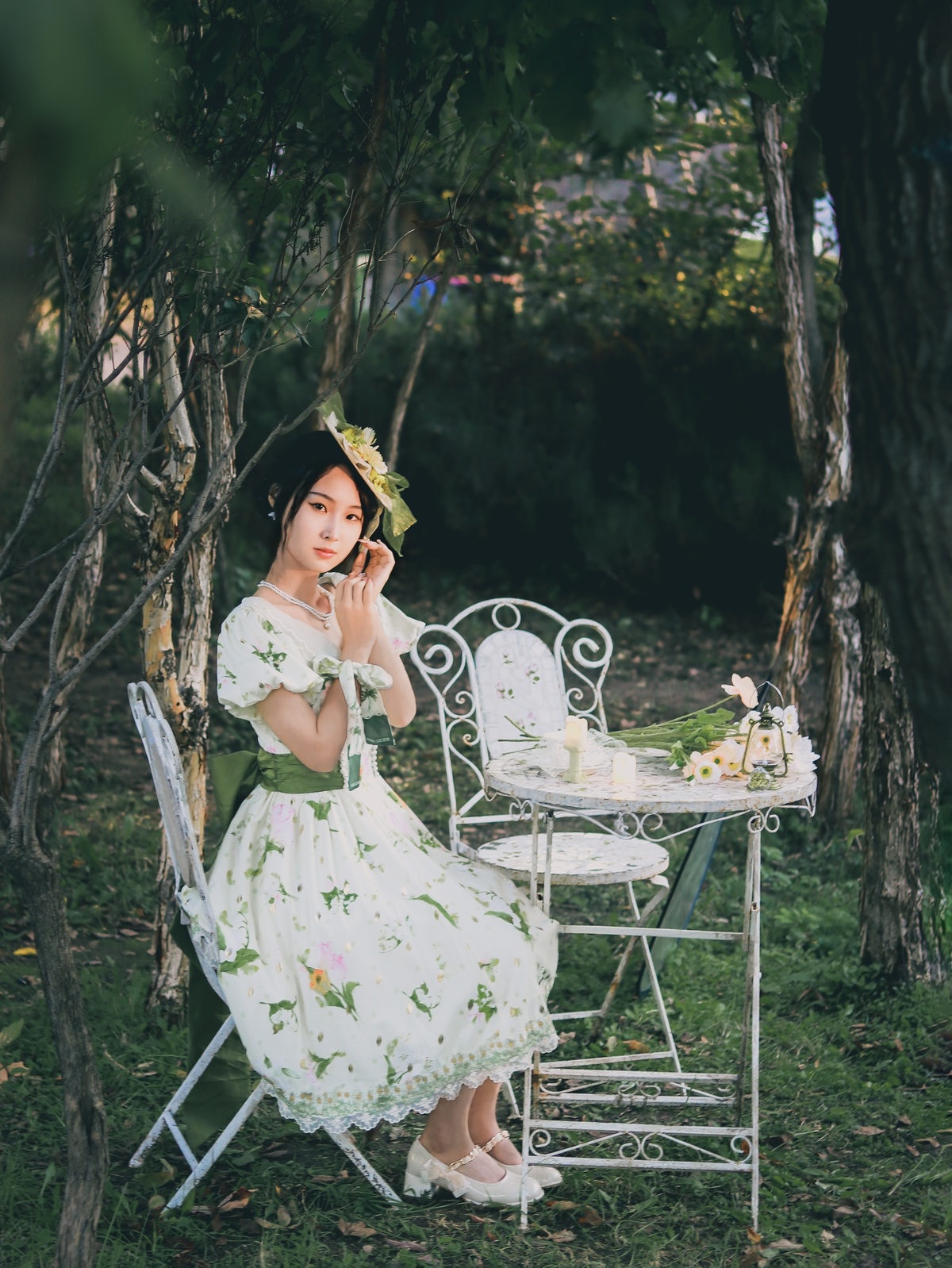 一位身穿白色连衣裙的年轻女子坐在花园里摆着鲜花的桌子旁打电话