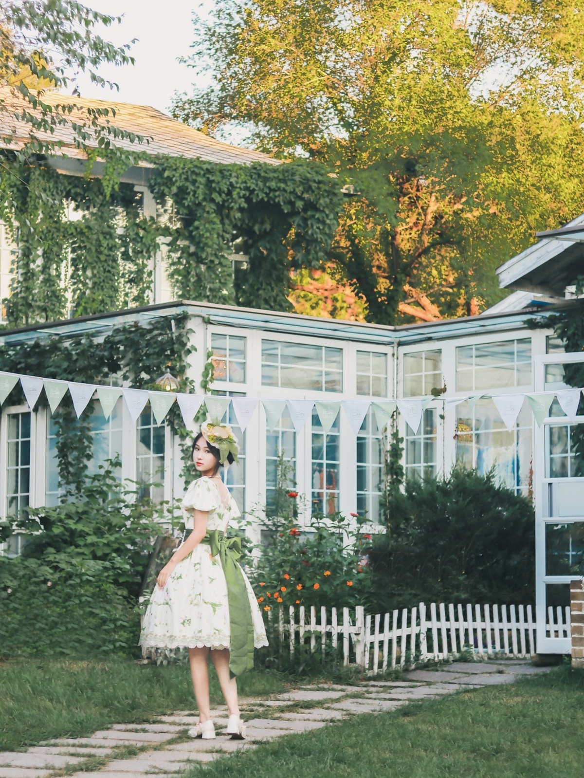 一个穿着绿色连衣裙的年轻女子穿过一个背景是白色房子的花园