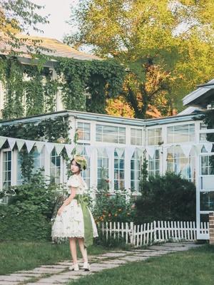 一个穿着绿色连衣裙的年轻女子穿过一个背景是白色房子的花园