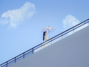 一个撑着伞的女人坐在屋顶上 头顶着一只鸟 映衬着蓝天