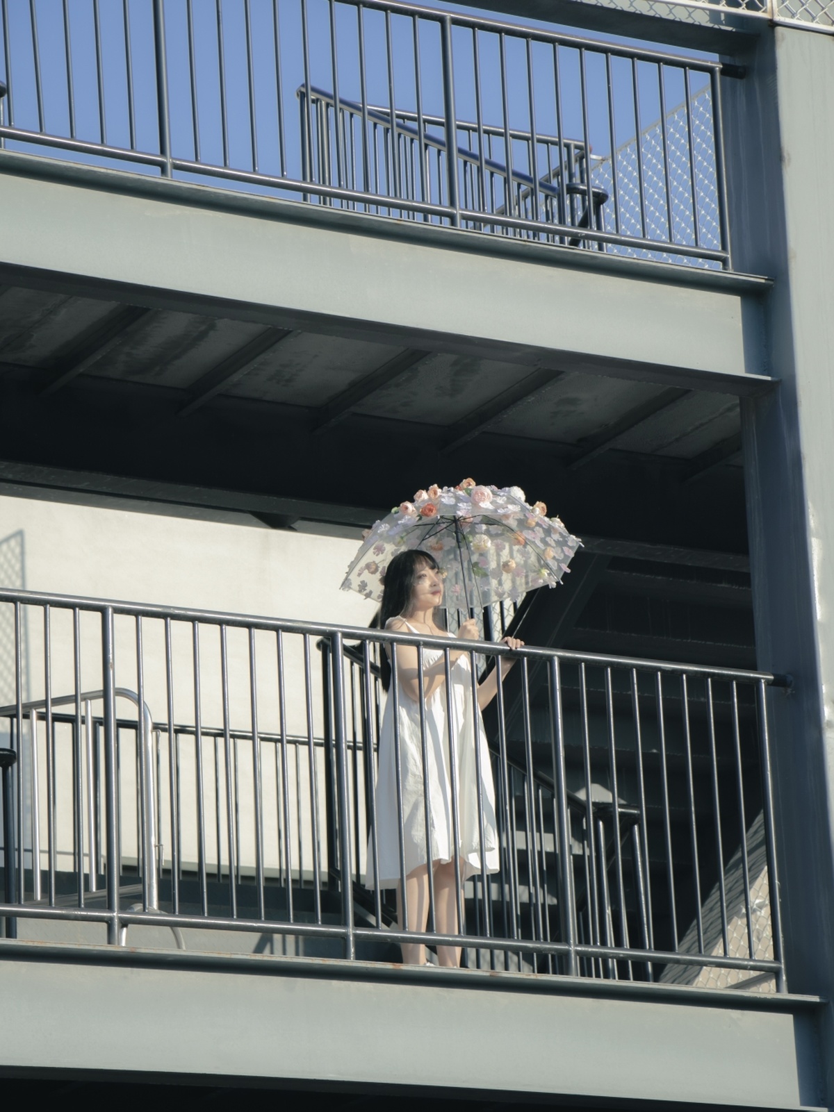 一个穿着白色连衣裙的女人撑着一把撑开的伞站在阳台上