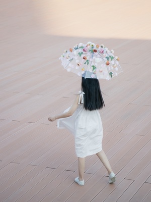 一个穿着白色连衣裙的年轻女子 头上拿着一把带花的伞
