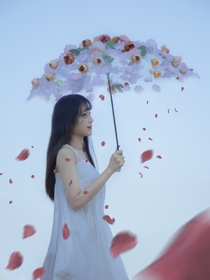一个穿着白色连衣裙的年轻女子拿着一把花瓣从伞里冒出来的伞