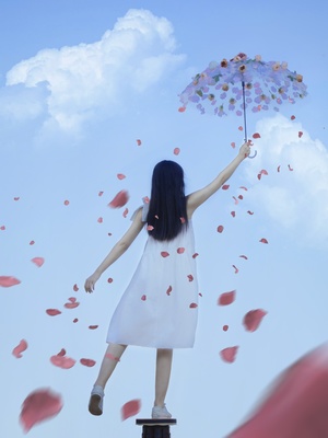 一位身穿白色连衣裙的年轻女子撑着一把伞 伞上飘着鲜花