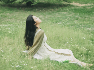 一位穿着美丽裙子的年轻女子坐在草地上 周围是花丛。