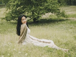 一个美丽的年轻女子穿着一件白色连衣裙坐在草地上鲜花丛中