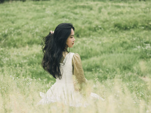 一个穿着白色连衣裙的年轻女子坐在绿色的草地上