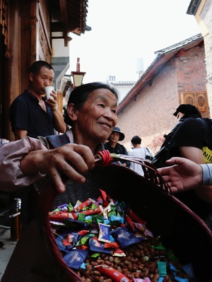 一个老太太正在街上市场的一个老人手中递一个装满零食的袋子。