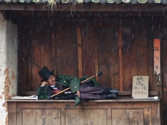 一些人正在一所建筑物的外面 在雨中睡觉 窗户是木制的 一个人躺在阳台上 手里拿着一把伞。